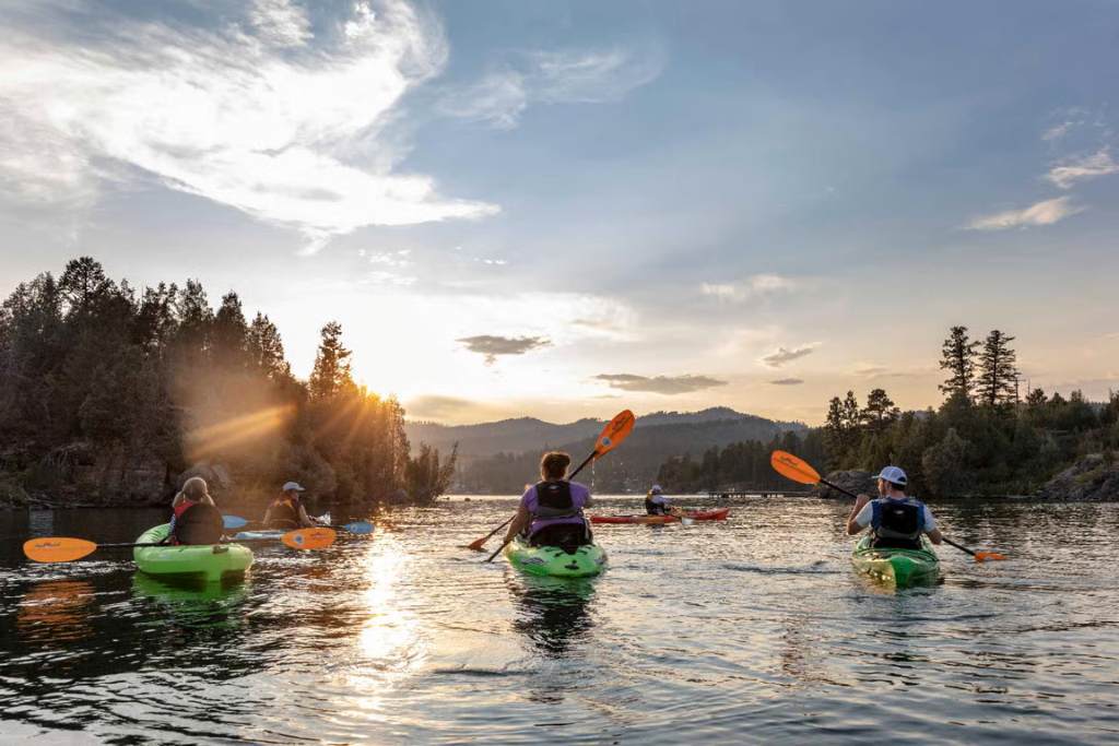 Family kayaking on Lake McDonald at sunset in Glacier National Park's West Entrance area.